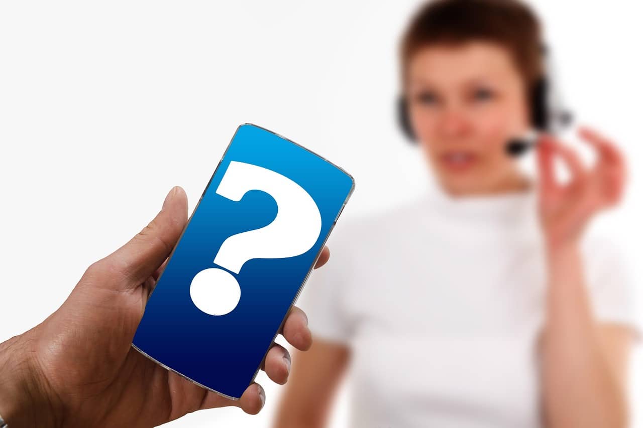 Persona al call center con cuffie e microfono, in primo piano uno smartphone con punto interrogativo.