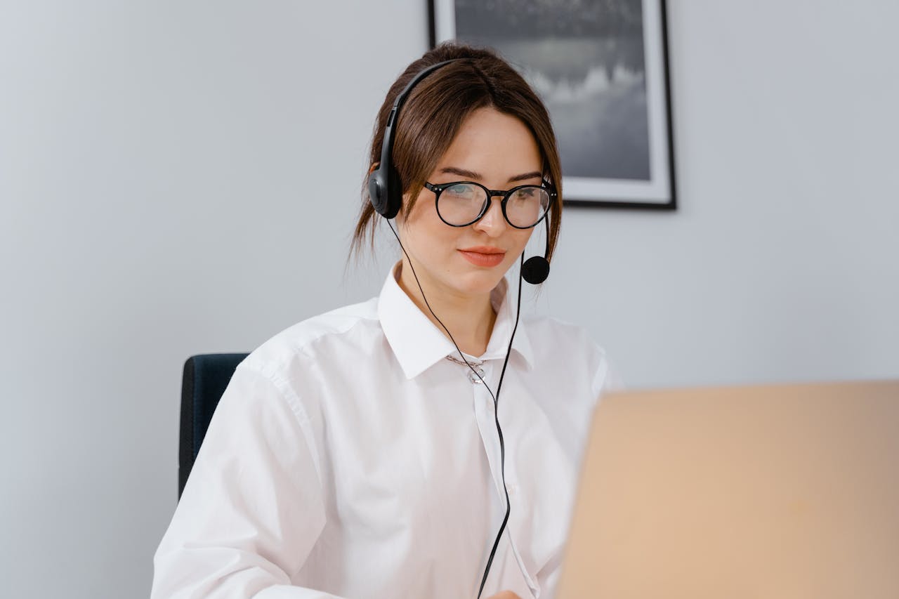 Operatrice di call center con cuffie e microfono lavora da remoto su laptop in un ambiente professionale moderno.